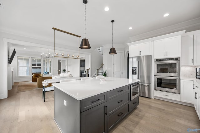 kitchen with white cabinetry, appliances with stainless steel finishes, a kitchen island, pendant lighting, and light hardwood / wood-style floors