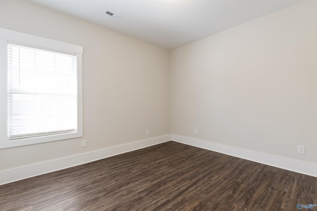 empty room with dark wood-type flooring, visible vents, and baseboards