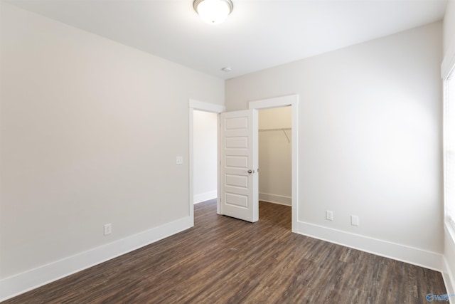 unfurnished bedroom with dark wood-type flooring, a closet, a spacious closet, and baseboards