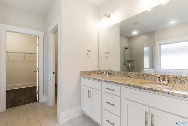 full bathroom with tiled shower, a sink, a walk in closet, and tile patterned floors