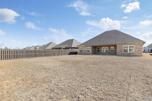 back of property with brick siding, a shingled roof, and fence