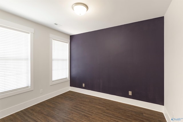 unfurnished room featuring dark wood-style floors, an accent wall, and baseboards