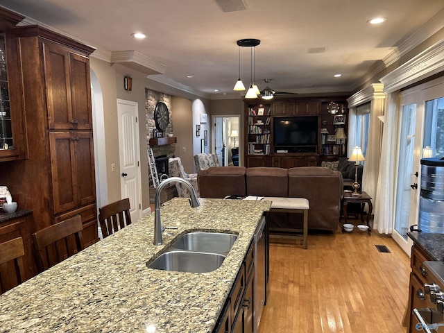 kitchen with a stone fireplace, crown molding, light wood-style flooring, and a sink