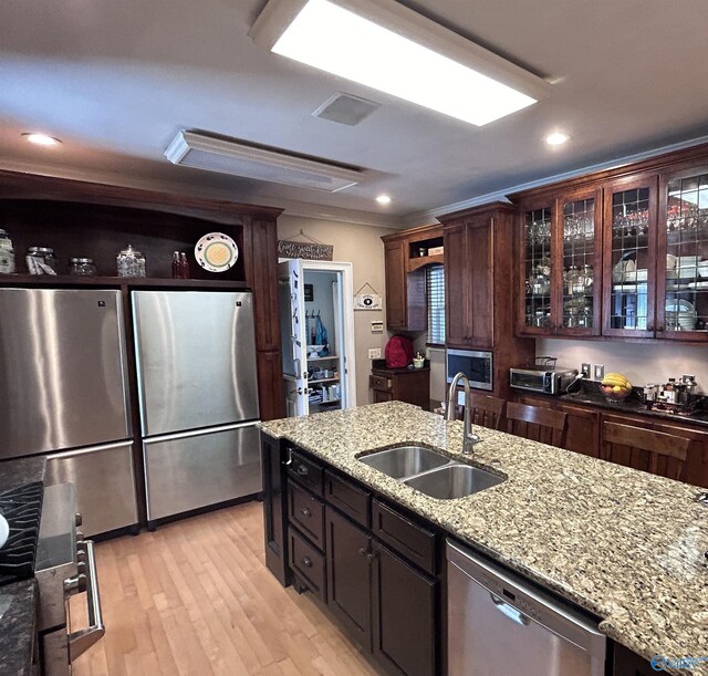 kitchen with light stone countertops, dark brown cabinets, light hardwood / wood-style flooring, stainless steel appliances, and sink