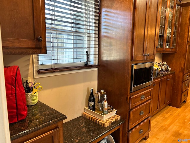 kitchen with light hardwood / wood-style flooring, dark stone counters, and stainless steel microwave