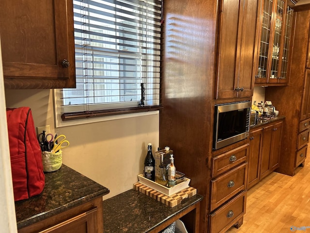 kitchen with dark stone countertops, stainless steel microwave, light wood-type flooring, and glass insert cabinets