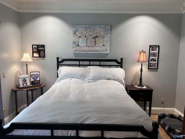 bedroom featuring a baseboard heating unit, baseboards, wood finished floors, and ornamental molding