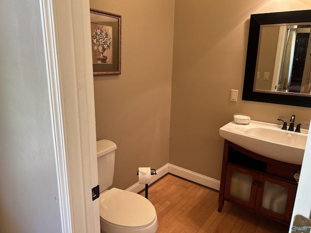 half bathroom with vanity, toilet, wood finished floors, and baseboards