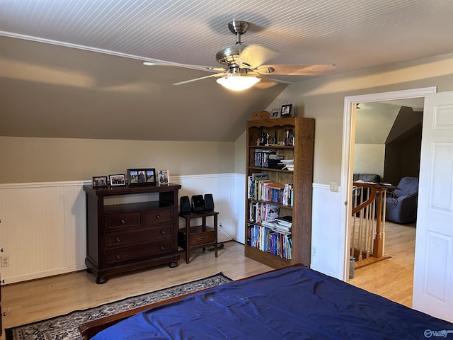 bedroom with wainscoting, a ceiling fan, lofted ceiling, and light wood-style floors