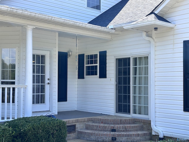 entrance to property with a porch and a shingled roof