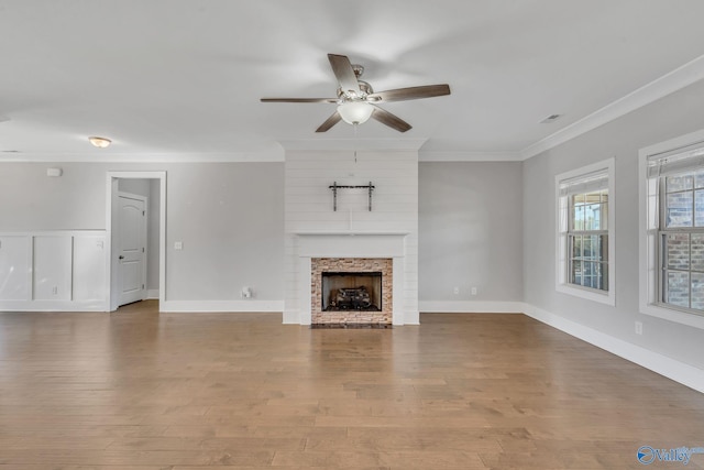 unfurnished living room with ornamental molding, wood-type flooring, a large fireplace, and ceiling fan