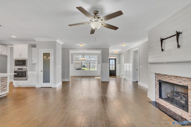 unfurnished living room with ornamental molding, a fireplace, wood-type flooring, and ceiling fan with notable chandelier