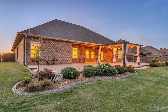 back house at dusk featuring a patio and a lawn