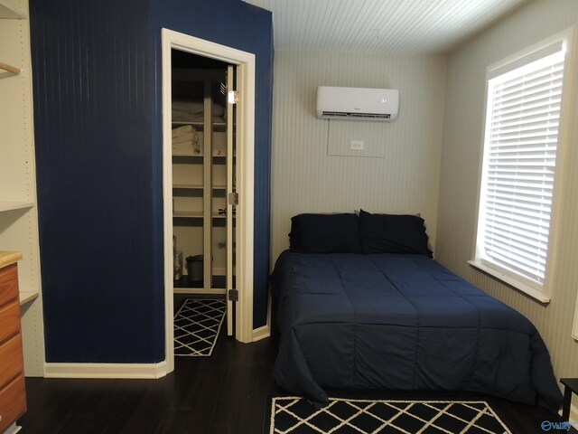 bedroom featuring a wall mounted AC, wood finished floors, baseboards, and multiple windows