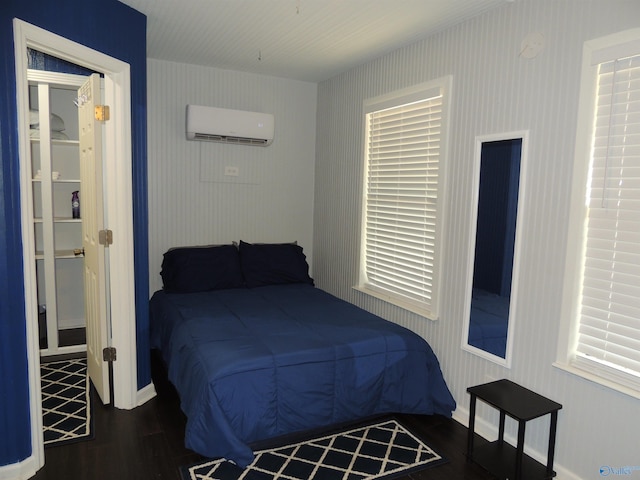 bedroom with a wall mounted AC, wood finished floors, and baseboards