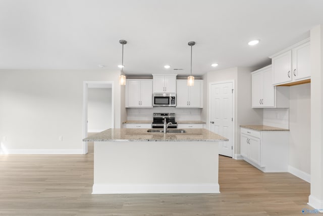 kitchen with a sink, white cabinets, appliances with stainless steel finishes, a center island with sink, and pendant lighting