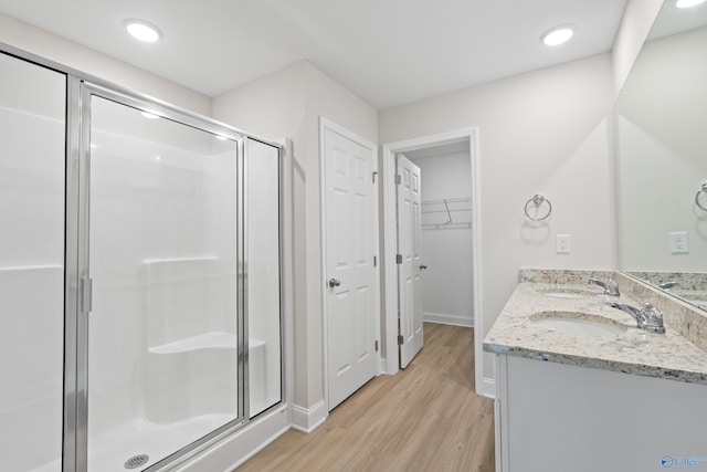 bathroom with a sink, a spacious closet, wood finished floors, and a shower stall