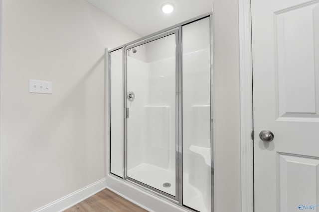 bathroom with wood finished floors, a shower stall, and baseboards