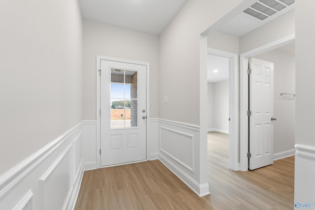 doorway with light wood finished floors, visible vents, a decorative wall, and wainscoting