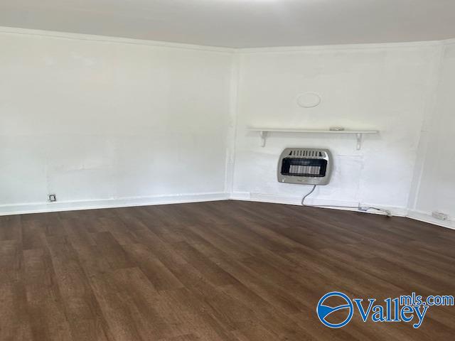 unfurnished living room with wood finished floors, heating unit, crown molding, and baseboards