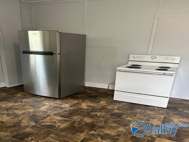 kitchen featuring stone finish floor, white range with electric cooktop, freestanding refrigerator, and baseboards