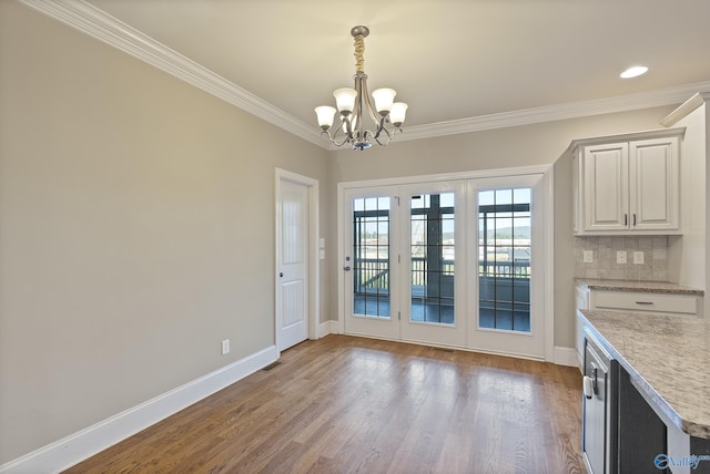 unfurnished dining area featuring baseboards, visible vents, ornamental molding, wood finished floors, and a chandelier