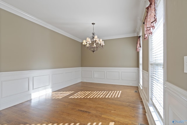 unfurnished room featuring a chandelier, light wood-style floors, wainscoting, and crown molding