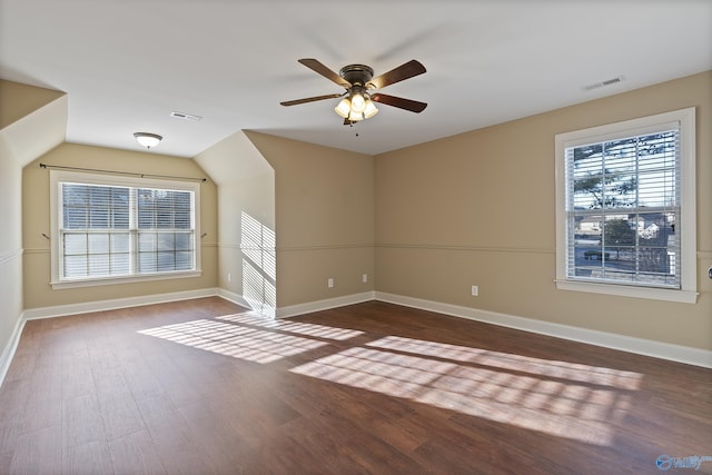 empty room with a wealth of natural light, visible vents, lofted ceiling, and wood finished floors