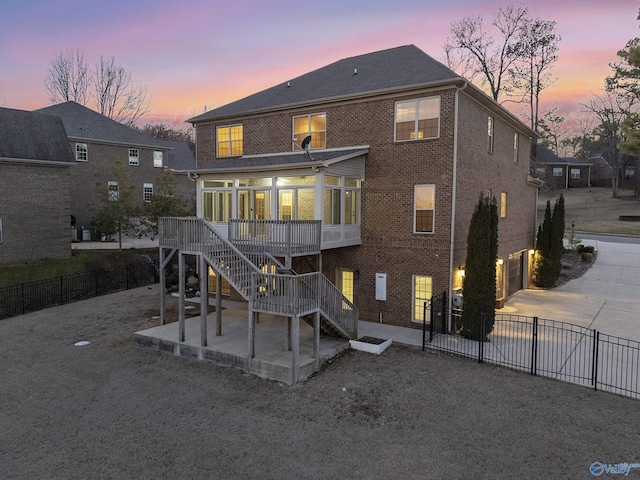 back of property at dusk with brick siding, fence, stairs, concrete driveway, and a patio area