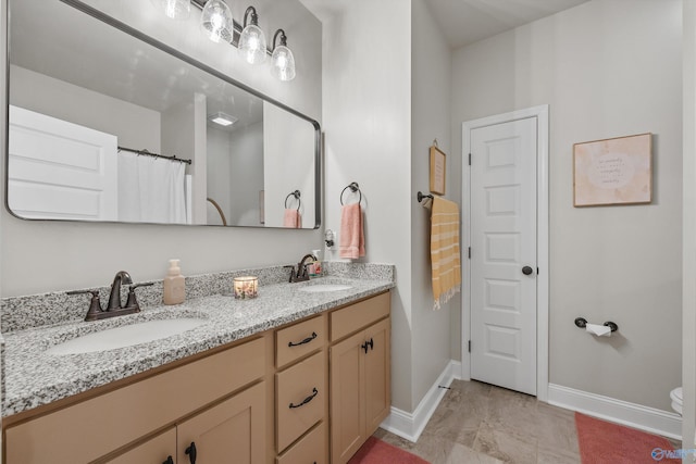 bathroom with toilet, double vanity, a sink, and baseboards