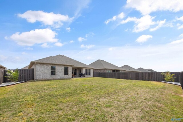 rear view of property with brick siding, a fenced backyard, and a lawn