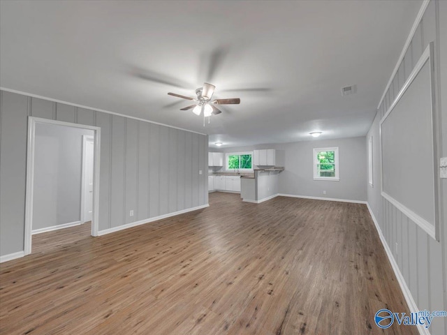 unfurnished living room featuring ceiling fan, a decorative wall, wood finished floors, and visible vents