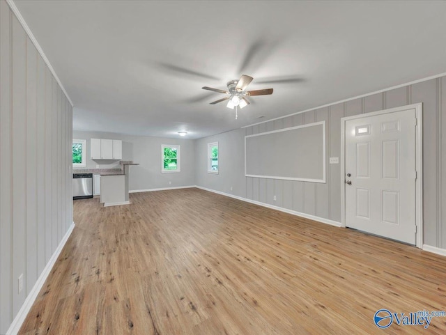 unfurnished living room with ornamental molding, a decorative wall, baseboards, light wood-type flooring, and a ceiling fan