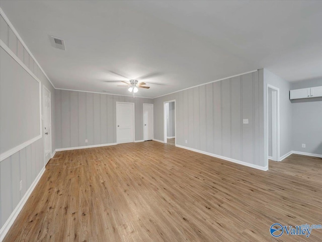 interior space featuring visible vents, a ceiling fan, light wood-style floors, and a decorative wall
