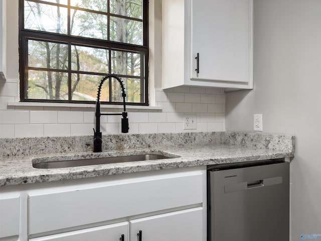 kitchen with light stone countertops, white cabinetry, stainless steel dishwasher, and sink