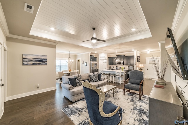 living room featuring dark hardwood / wood-style flooring, ceiling fan with notable chandelier, a tray ceiling, crown molding, and wooden ceiling