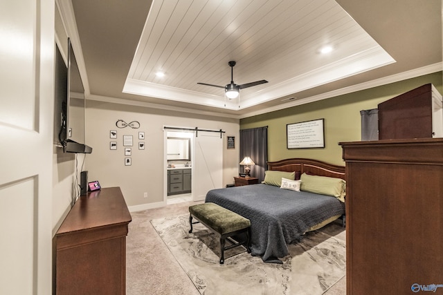 carpeted bedroom with ceiling fan, a barn door, a raised ceiling, and ensuite bathroom