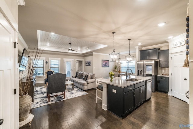 kitchen with dark wood-type flooring, a raised ceiling, stainless steel dishwasher, a center island with sink, and ceiling fan with notable chandelier