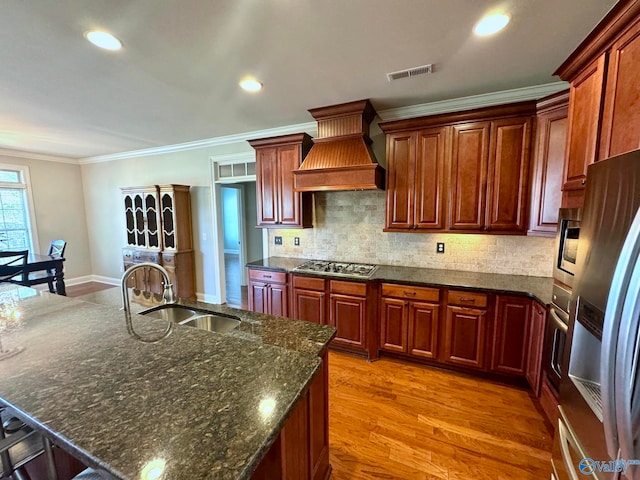 kitchen featuring premium range hood, ornamental molding, stainless steel appliances, light wood-type flooring, and sink