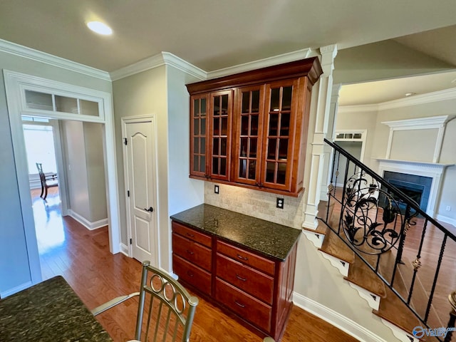 kitchen featuring tasteful backsplash, ornamental molding, dark hardwood / wood-style flooring, dark stone countertops, and decorative columns