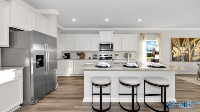 kitchen with light stone countertops, a center island with sink, white cabinets, and appliances with stainless steel finishes