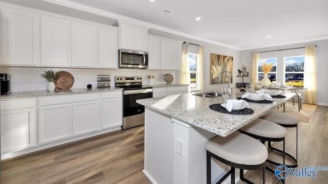 kitchen with hardwood / wood-style floors, a kitchen island with sink, sink, white cabinetry, and stainless steel appliances