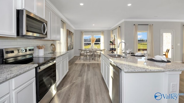 kitchen featuring light stone countertops, stainless steel appliances, a kitchen island with sink, sink, and white cabinetry