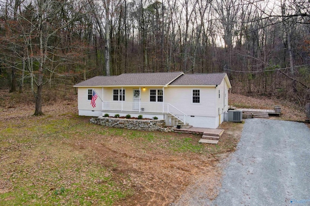 view of front of home featuring driveway, a forest view, covered porch, crawl space, and central AC unit