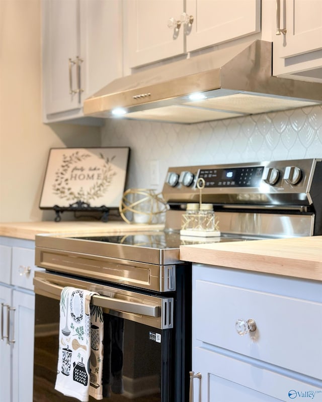 kitchen with stainless steel electric range, butcher block countertops, under cabinet range hood, white cabinetry, and backsplash