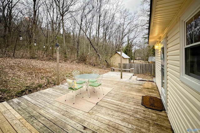 wooden terrace featuring an outbuilding, outdoor dining space, and fence