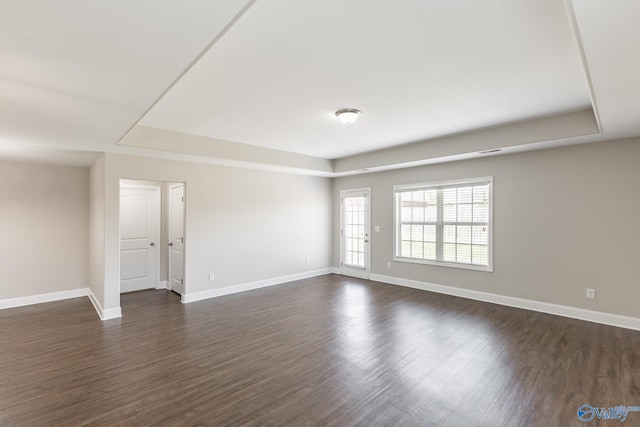 spare room featuring a tray ceiling, dark wood-style flooring, and baseboards