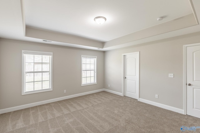 empty room with a tray ceiling, carpet, visible vents, and baseboards