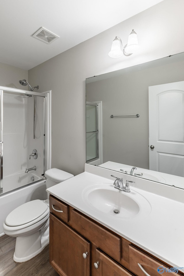 full bathroom featuring vanity, visible vents, toilet, wood finished floors, and combined bath / shower with glass door