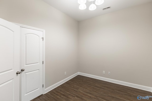 empty room featuring a notable chandelier, visible vents, baseboards, and dark wood-style floors